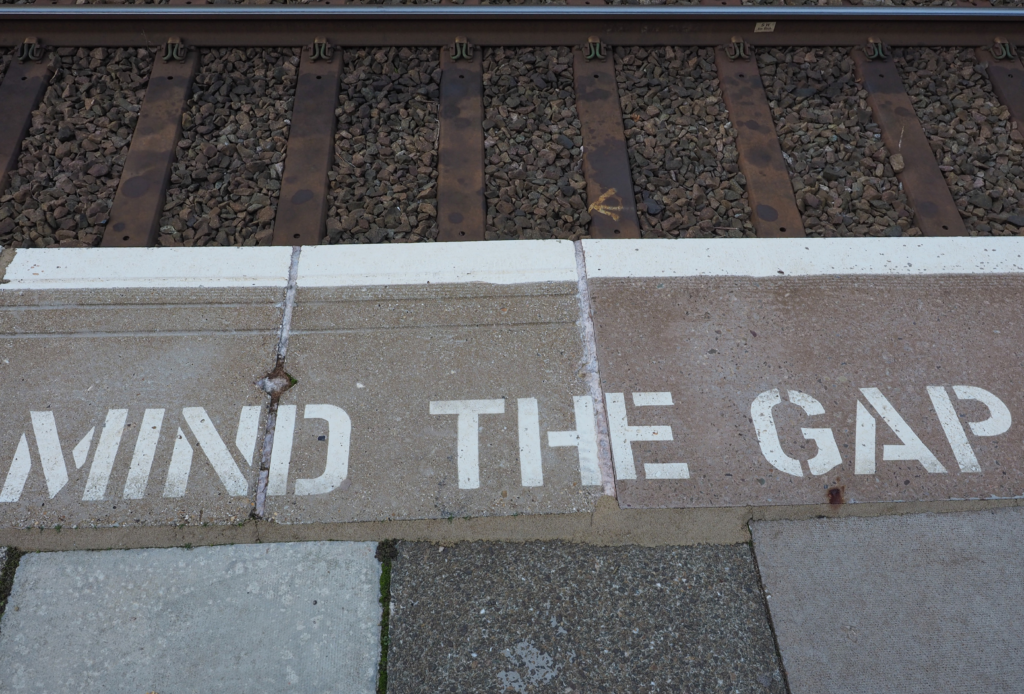 A railway on the top and part of a sidewalk showing the statement "mind the gap".