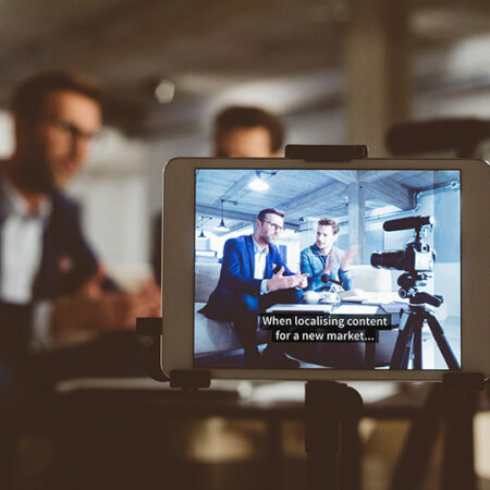 A tablet on the front recording two mean seating on a coach and having a conversation.